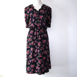 May include: A vintage black dress with a floral pattern of pink and red roses. The dress has short sleeves, a v-neckline, and a gathered waist. The dress is displayed on a white mannequin.