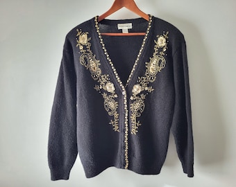 May include: Black cardigan sweater with gold floral embroidery and sequin accents. The V-neck sweater has long sleeves and is buttoned down the front. The sweater is hanging on a wooden hanger.