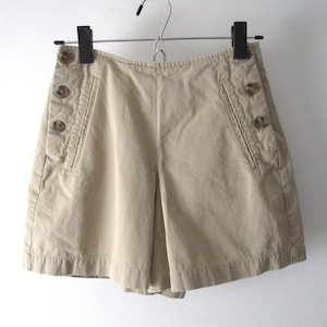 May include: Beige cotton shorts with a button-up front and side pockets. The shorts have a relaxed fit and a casual style.