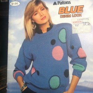 Può includere: Un maglione blu a maglia con un motivo a pois colorati. Il maglione ha un collo rotondo e maniche lunghe. Il motivo include pois rosa, verdi e neri.