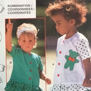 Puede incluir: Dos niñas pequeñas con vestidos blancos y verdes con dobladillo con volantes. Los vestidos tienen botones rojos y uno tiene una aplicación de oso verde. El texto "KOMBINATION / COORDONNEES / COORDINATES" es visible en el fondo.