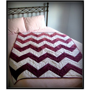 Pode incluir: Uma cama com colcha e almofadas rosa, coberta com um edredom feito à mão. O edredom apresenta um padrão de chevron arrojado em branco e bordô. O texto "Chevrons!!!" está no topo da imagem.