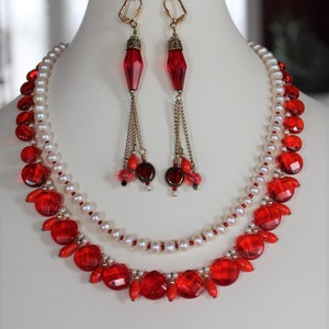 May include: A two-strand necklace with red faceted beads and white pearls. The necklace is paired with matching earrings with red faceted beads and gold chains.
