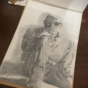 May include: A black and white pencil drawing of a person wearing glasses and sitting with their legs crossed. The drawing is on a white sheet of paper.