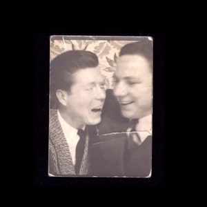 May include: Black and white photo of two men laughing together. The men are wearing suits and ties. The photo is slightly faded and has a vintage look.