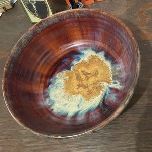 May include: A large, round ceramic bowl with a deep red glaze. The bowl has a swirling pattern of blue and white glaze in the center.