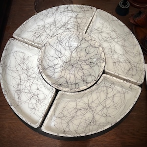 May include: A white ceramic serving dish set with a central bowl and five surrounding compartments. Each piece is decorated with a black, abstract scribble pattern. The set is designed for serving snacks or appetizers.