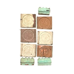 May include: An assortment of antique wooden architectural elements. The pieces feature a circular floral design within a square frame, with varying shades of brown and cream. Two smaller, green, decorative pieces are also present.