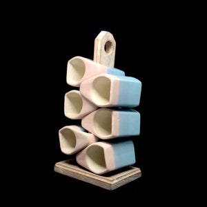 May include: A wooden stand with six ceramic mugs stacked on top. The mugs are half pink and half blue.
