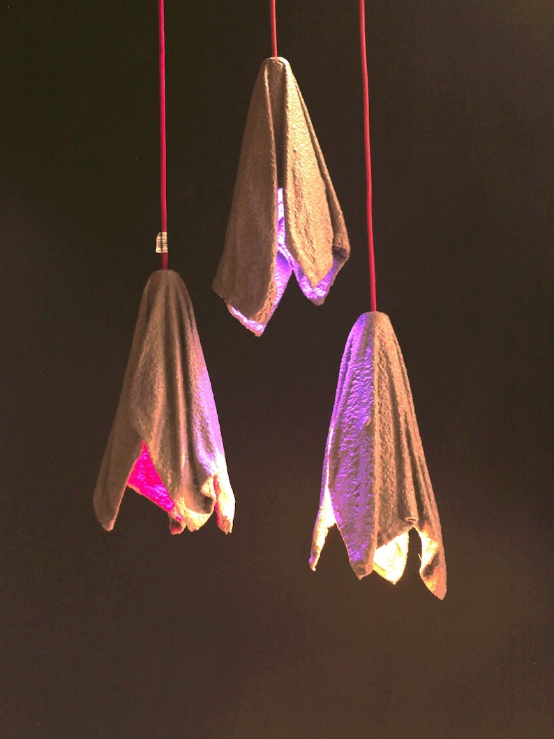 Pu&ograve; includere: Tre lampadari sospesi in carta marrone, ognuno con una forma unica e una luce viola che brilla attraverso.