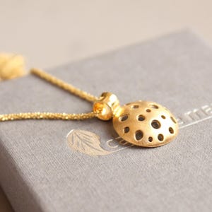 May include: A gold necklace with a round pendant featuring a delicate, intricate design of small circles. The pendant is on a gray surface with the word "Carney" printed on it.