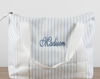 May include: A blue and white striped tote bag with white handles and the name "Madison" embroidered in a script font. The bag is sitting on a wooden surface.