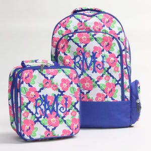 May include: A matching backpack and lunch bag set. Both items feature a white background with a pink floral pattern, green leaves, and a blue trellis design. The backpack and lunch bag have blue trim and embroidered initials.