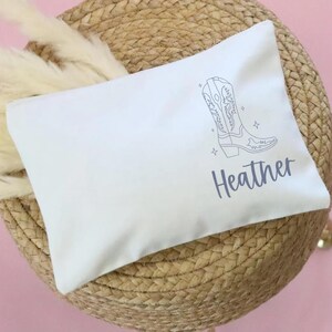 May include: White cotton makeup bag with a line drawing of a cowboy boot and the name "Heather" printed in gray.