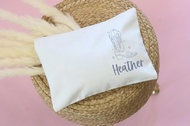 May include: White cotton makeup bag with a line drawing of a cowboy boot and the name "Heather" printed in gray.