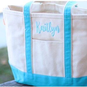 May include: A white canvas tote bag with blue trim and a personalized embroidered name, "Kaitlynn".