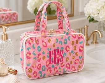 May include: A rectangular cosmetic bag with two top handles, featuring a vibrant pink, teal, and gold leopard print pattern. The front of the bag is embroidered with the monogram letters EES in a bold, dark pink thread, finished with white piping.
