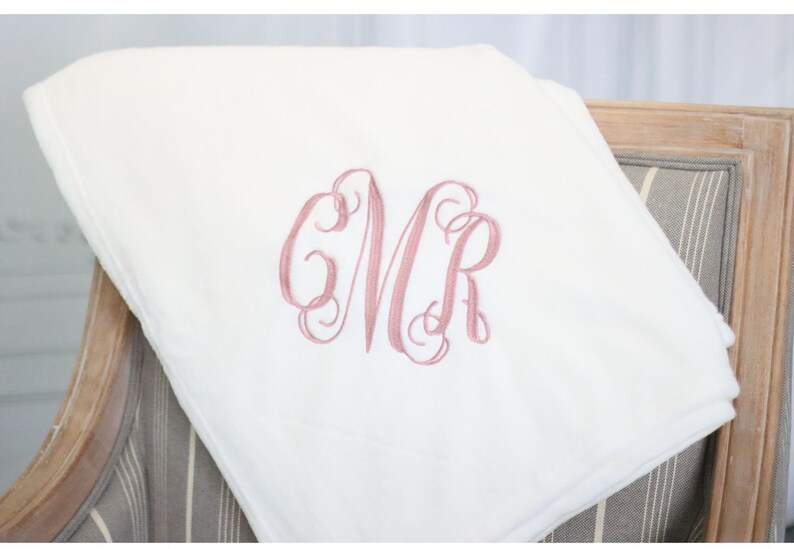 May include: White plush throw blanket with a pink embroidered monogram "CMR" in a script font.