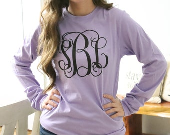 May include: A lavender long-sleeved t-shirt with a black monogram "SBL" on the front.