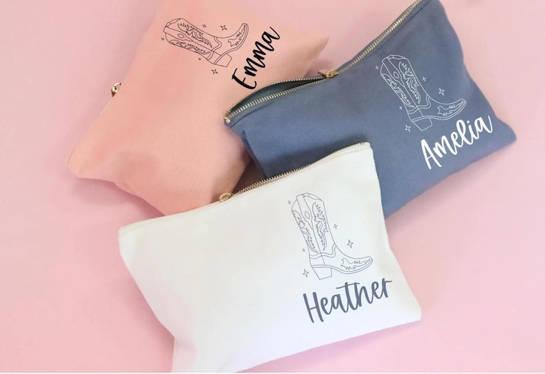 May include: Three white canvas zippered pouches with a black line drawing of a cowboy boot and a name on each pouch. The names are Emma, Amelia, and Heather.