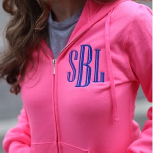May include: A bright pink zip-up hoodie with a blue embroidered monogram "SBL" on the front.