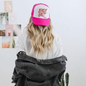 Puede incluir: Gorra de camionero rosa y blanca con la palabra "EASY" y un gr&aacute;fico de tigre. La gorra tiene una parte trasera de malla y una visera curva. La gorra la lleva una persona con el pelo largo y rubio.