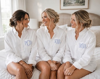 Op de afbeelding: Drie witte overhemden met knoopsluiting, lange mouwen en opgerolde manchetten. Elk overhemd heeft een lichtblauw geborduurd monogram op de linkerborstzak, met de letters PCD, KML en MVA in een schreeflettertype.