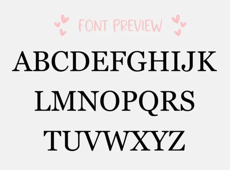 Op de afbeelding: Een lettertypevoorbeeld met het Engelse alfabet in hoofdletters in een zwart schreeflettertype. De tekst FONT PREVIEW staat bovenaan in het midden, geflankeerd door kleine roze hartjes aan beide kanten, op een witte achtergrond.