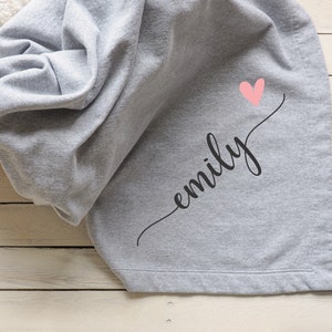 May include: A gray fleece blanket with the name "emily" written in black cursive script and a pink heart above the name.