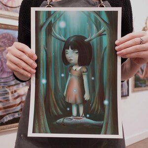 May include: A print of a surreal illustration featuring a young girl with deer antlers standing in a forest. The artwork has a muted color palette with shades of teal, brown, and peach. The girl is the focal point, with a somber expression.