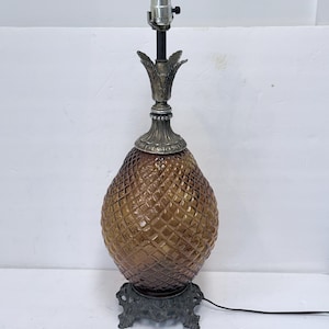 May include: A vintage table lamp with a brown, pineapple-shaped glass body and a decorative metal base. The lamp features a diamond-patterned texture on the glass and a silver-toned metal top with a bulb socket. The base has an ornate, floral design.