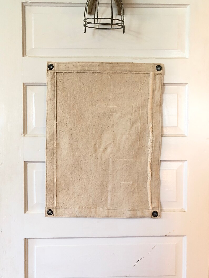 May include: A plain, off-white canvas banner with grommets in each corner. The banner is hanging on a white door.