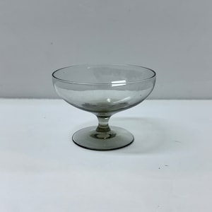 May include: A clear glass stemmed dessert dish with a wide bowl and a short stem. The dish is slightly tinted a light gray color.
