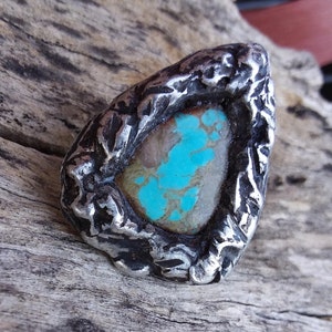 May include: A turquoise gemstone set in a silver ring with a rough, textured design.
