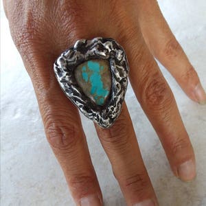 May include: A silver ring with a turquoise stone set in a textured, triangular setting.