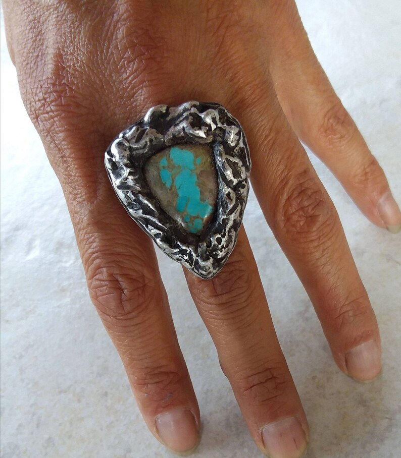 May include: A silver ring with a turquoise stone set in a textured, triangular setting.