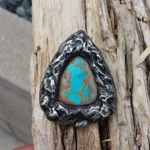May include: A turquoise gemstone set in a silver triangular pendant with a textured, hammered finish.