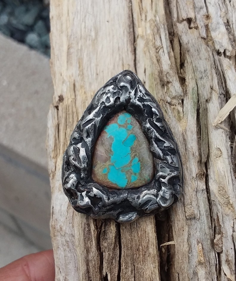 May include: A turquoise gemstone set in a silver triangular pendant with a textured, hammered finish.