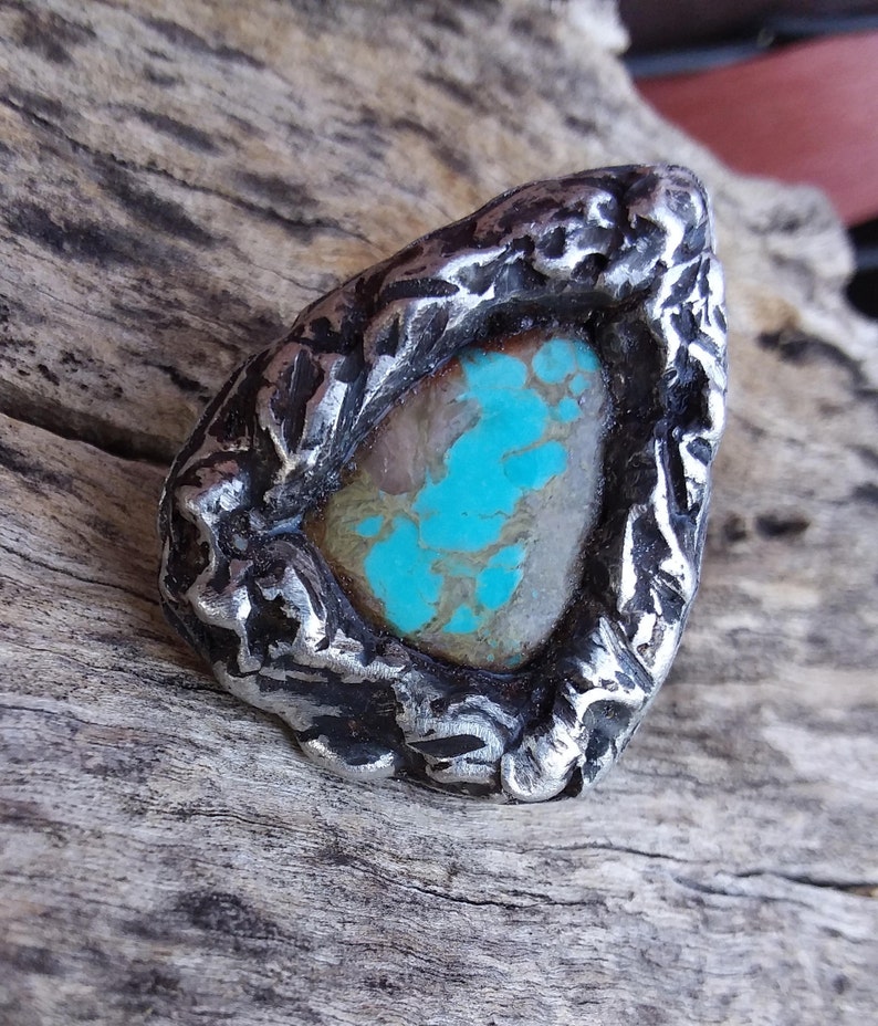 May include: A turquoise gemstone set in a silver ring with a rough, textured design.
