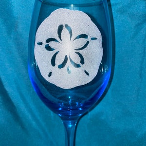 May include: A blue glass wine glass with a white sand dollar design etched into the side.