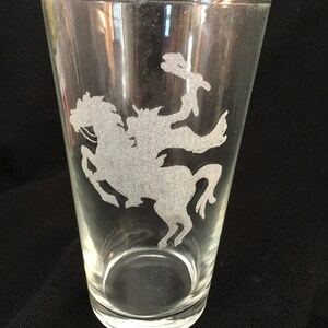 May include: A clear glass pint glass with an etched design of a cowboy riding a horse.