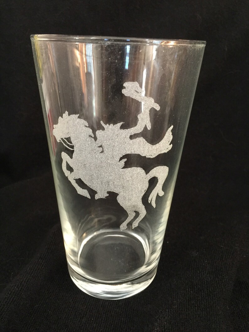 May include: A clear glass pint glass with an etched design of a cowboy riding a horse.