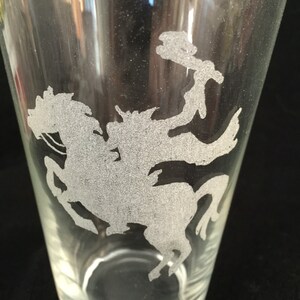 May include: A clear glass pint glass with a frosted etching of a knight riding a horse. The etching is in the center of the glass.