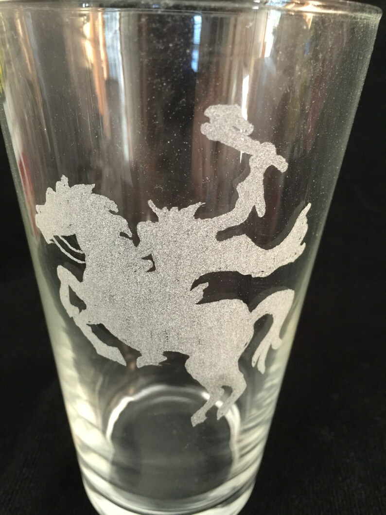 May include: A clear glass pint glass with a frosted etching of a knight riding a horse. The etching is in the center of the glass.