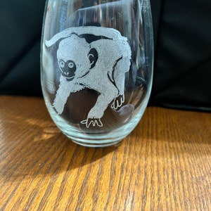 May include: A clear glass wine glass with an etched design of a white monkey. The monkey is facing the left side of the glass and has a long tail.