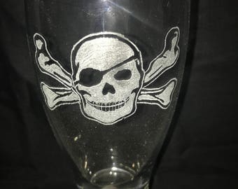 May include: A clear glass beer mug with an etched design of a skull and crossbones. The skull is wearing an eye patch.