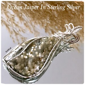 May include: A silver wire wrapped pendant featuring a green and white ocean jasper stone. The stone has a unique pattern of white dots and swirls.