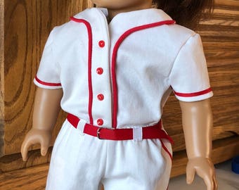 May include: A white baseball uniform with red trim and buttons for a doll. The doll has brown hair and green eyes.