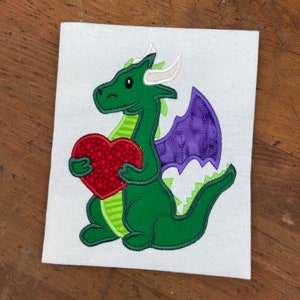 May include: Green dragon holding a red heart with white horns and purple wings.