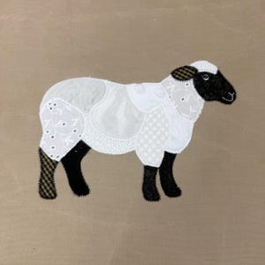 May include: A fabric appliqué of a sheep featuring a black head and legs with a white body composed of various patterned textile patches including floral eyelet, lace, and solid white fabric, creating a textured and layered appearance.